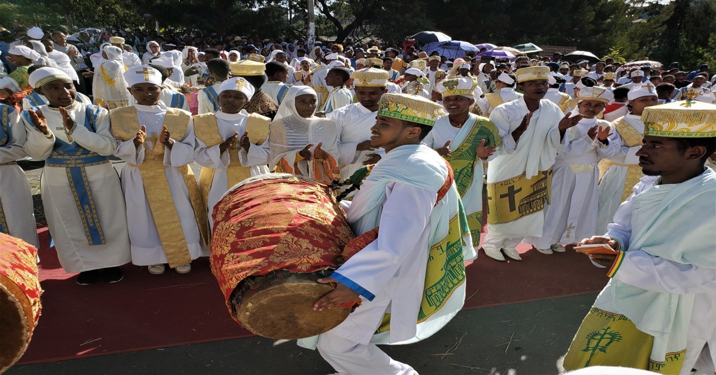 Individuals dressed in white attire performing a ritual with a drum